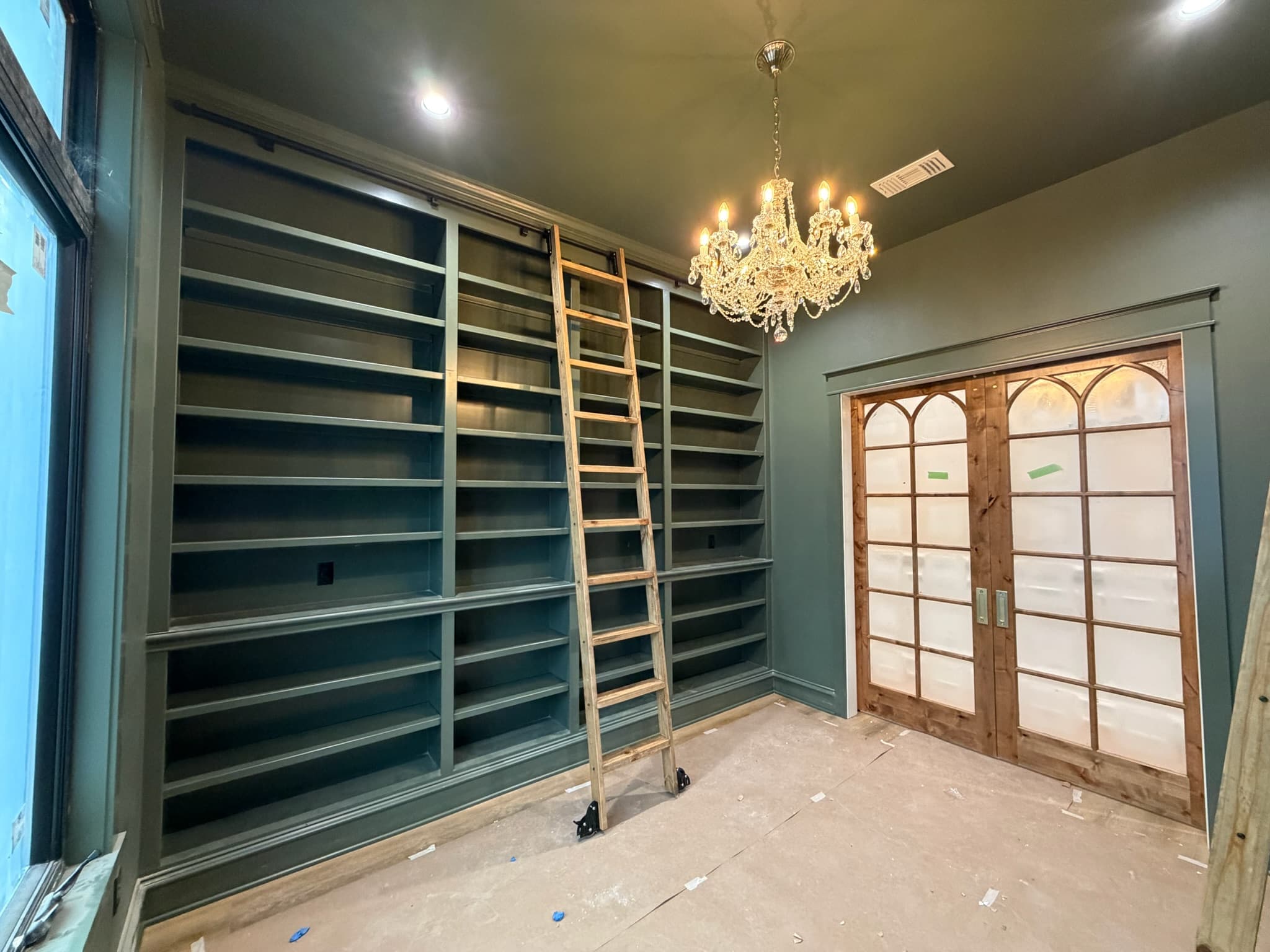 Custom library with floor to ceiling painted shelving, a rolling ladder and arched glazed doors