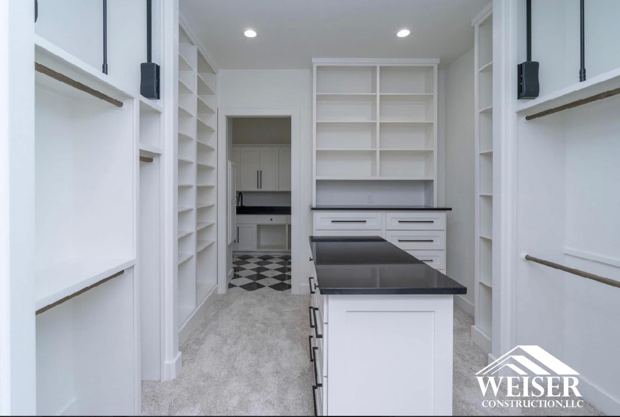 Primary closet build-out with floor to ceiling shelving and a stone topped island